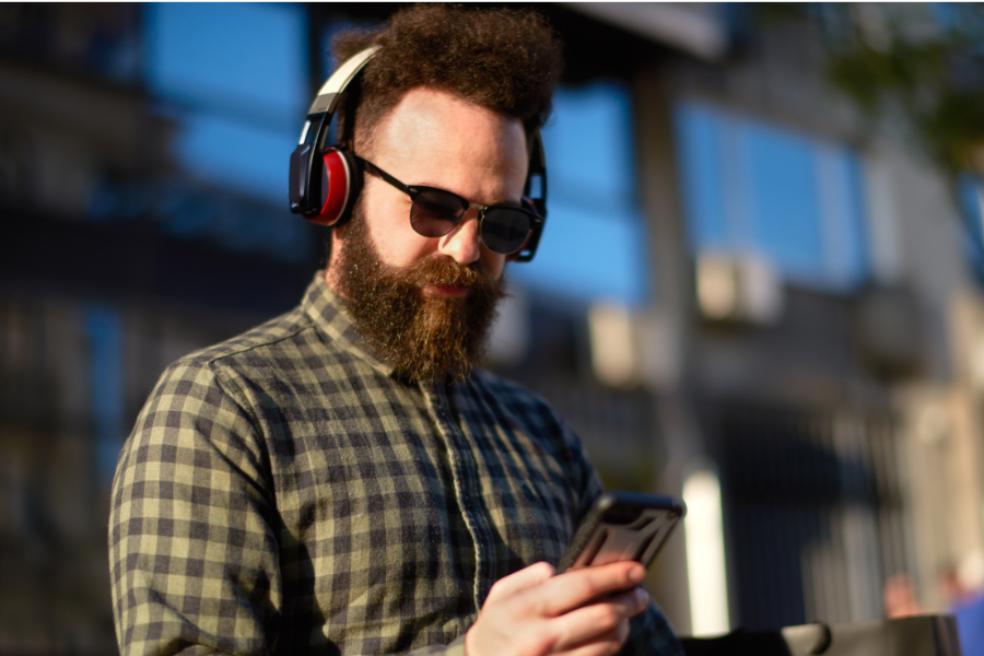 Stock image of a man with a visual impairment outside with headphones on, using a smartphone.