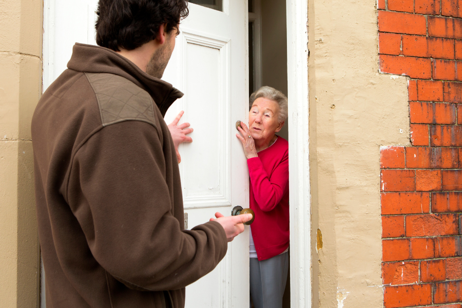 Stock image of a senior woman opening her door to talk to a man at the door.