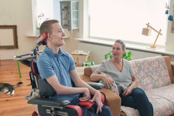 Get Help 25 1.png Stock photo of young man sitting in a power wheelchair next to a woman sitting on the couch.