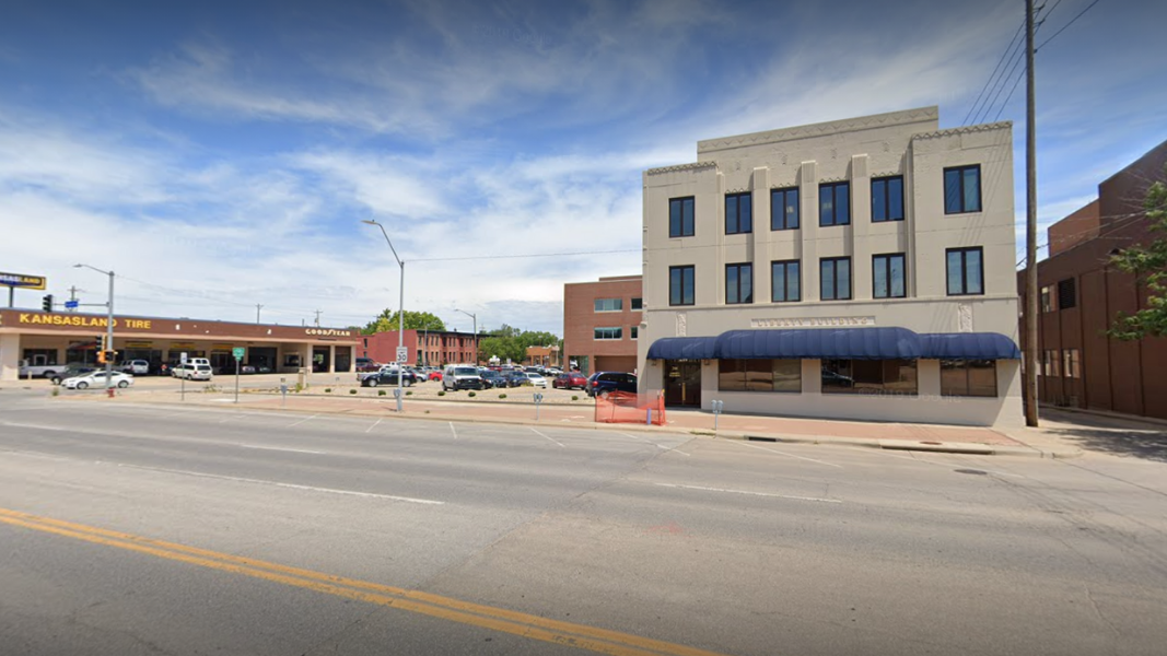 Image of DRC's office building form across the street. It is a three-story, beige building in the right of the image. Behind the building is a blue sky with some clouds. 