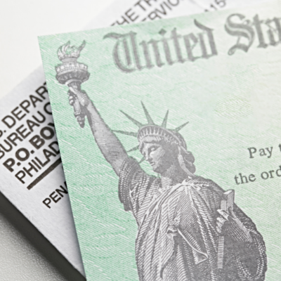 This is a close up image of a U.S. Treasury check on top of an envelope. A grayscale image of the Statue of Liberty is on the green check. 