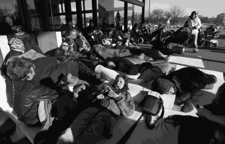 Black and white image of around 20 people laying outside of a city building.