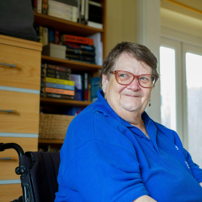 Stock photo of a woman sitting in a wheelchair in a home setting smiling and looking to the side. 