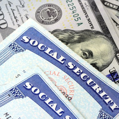This is a close up image of two Social Security cards on top of a 100 dollar American bill. On the cards, only the words “SOCIAL SECURITY” are visible.
